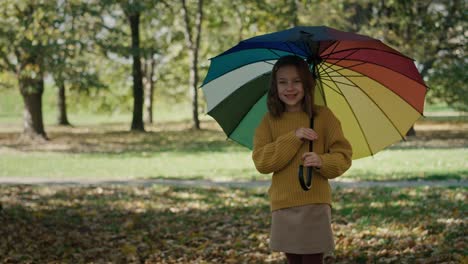 niña de pie en el parque con paraguas de colores durante el otoño.