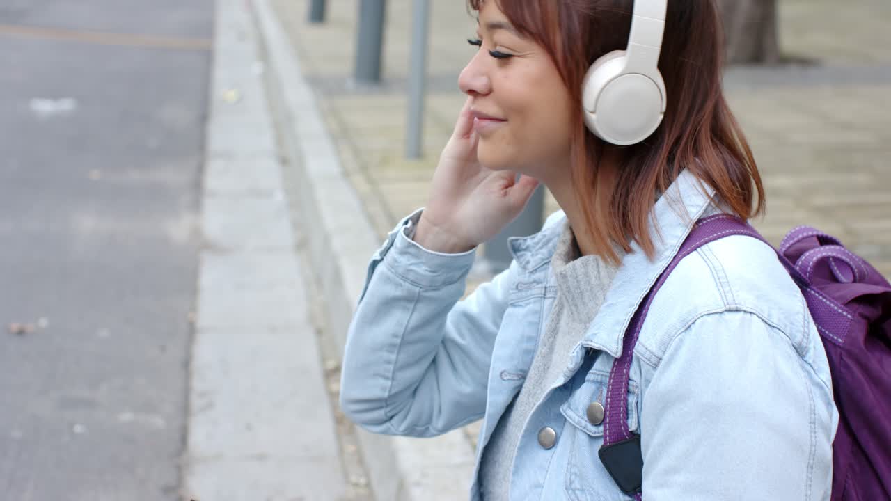 Sorridendo, una donna sta regolando le cuffie bianche su una panchina mentre scorre lo smartphone in cerca di musica.