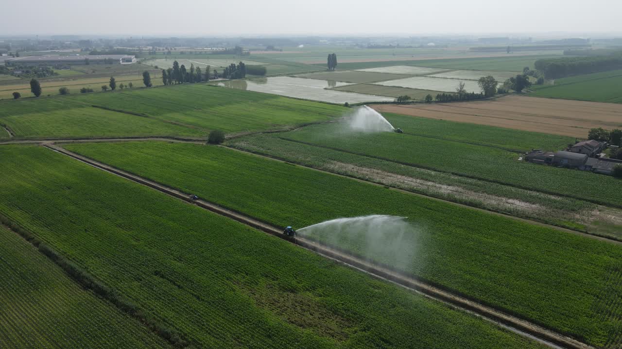 Drone footage showing a smooth aerial rotation around two tractors simultaneously irrigating farmland in the Po Valley (Pianura Padana), Italy