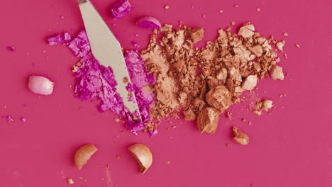 crushed makeup and tools on pink background
