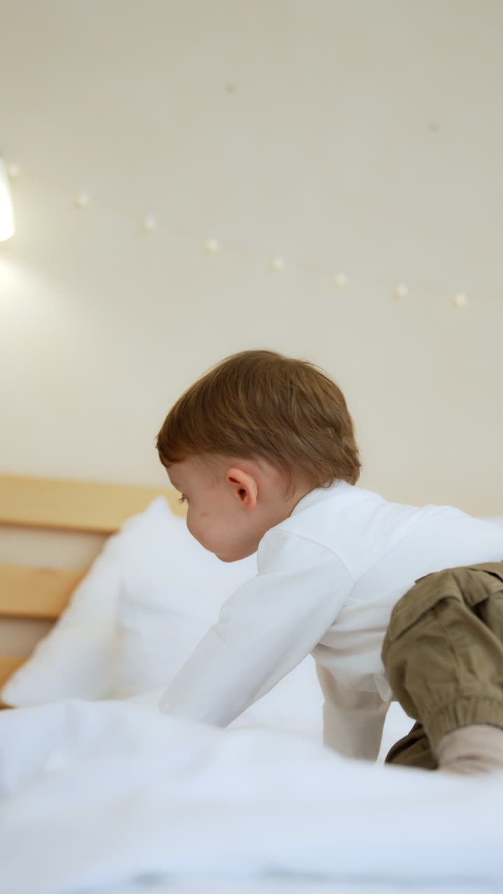 Small kid crawls by the bog double bed. Lovely toddler boy sits up and cries pointing at something. Vertical video.