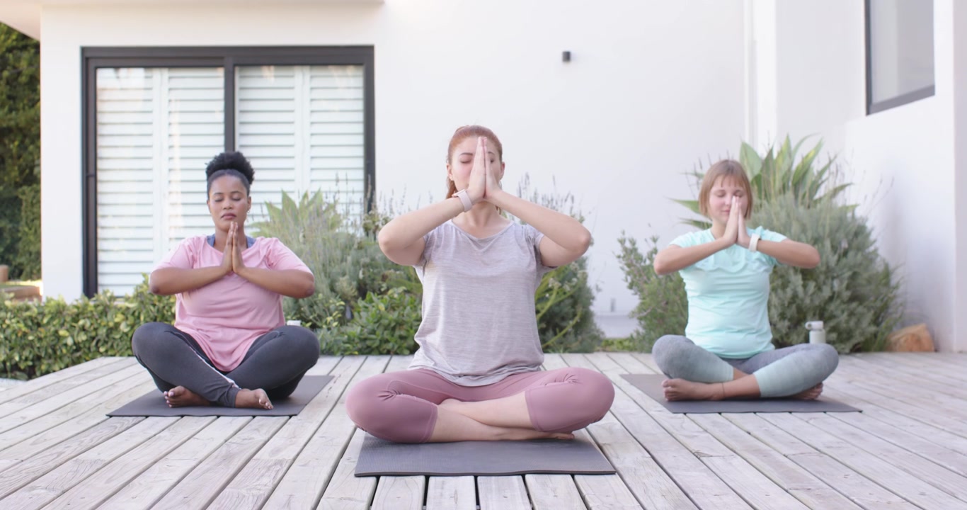 Forskellige kvindelige venner følger centerlederen, der sænker håndfladerne til brystet på dækmåtter til meditation.