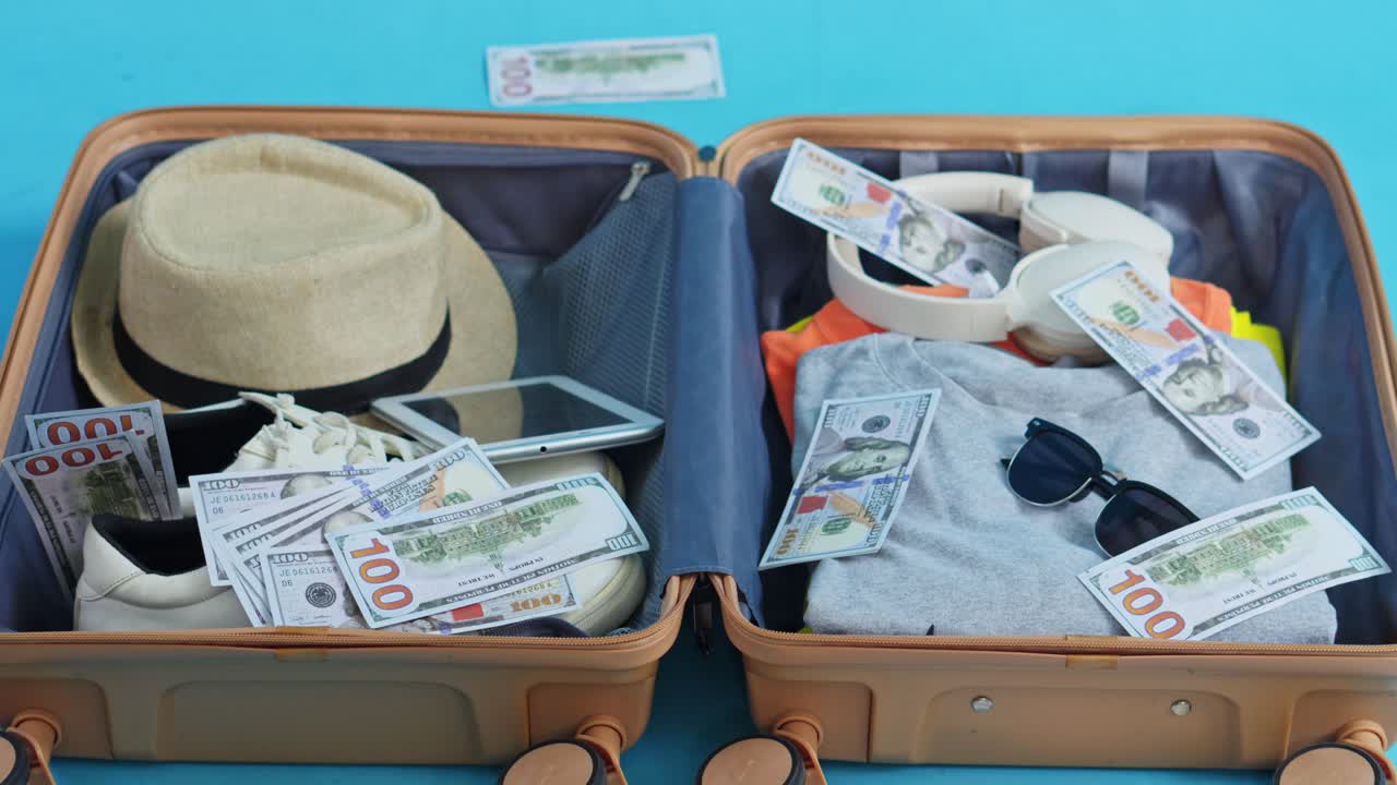 De l'argent tombant dans une valise ouverte remplie de vêtements d'été, de chaussures et d'accessoires de voyage