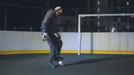 atleta en corredores casuales haciendo malabarismos con el fútbol hábilmente en la cancha al aire libre por la noche, escena de acción enfocada bajo luces brillantes con fondo urbano, marcas de límite amarillas y postes de portería