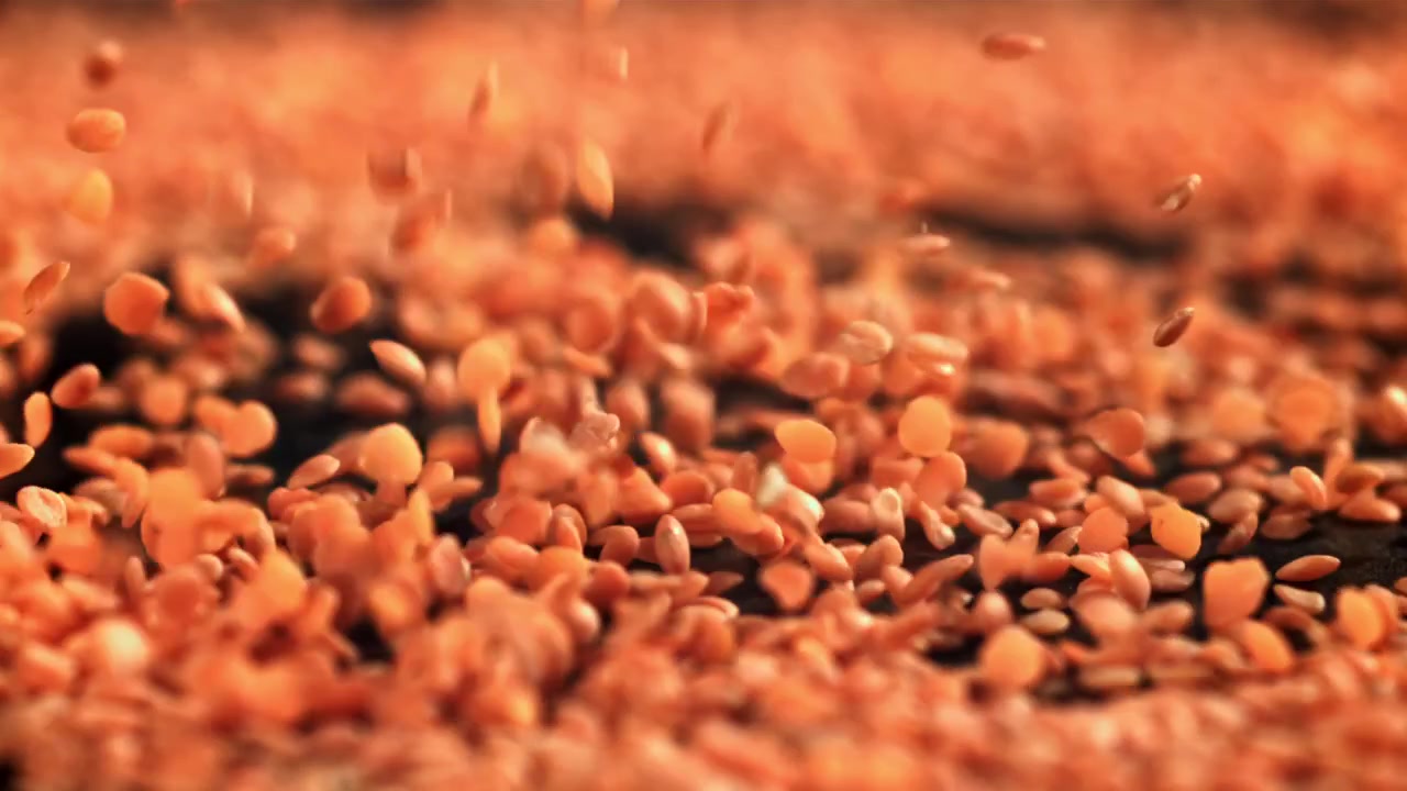 Lenticchie Rosse che Cadono al Rallentatore su una Superficie Scura