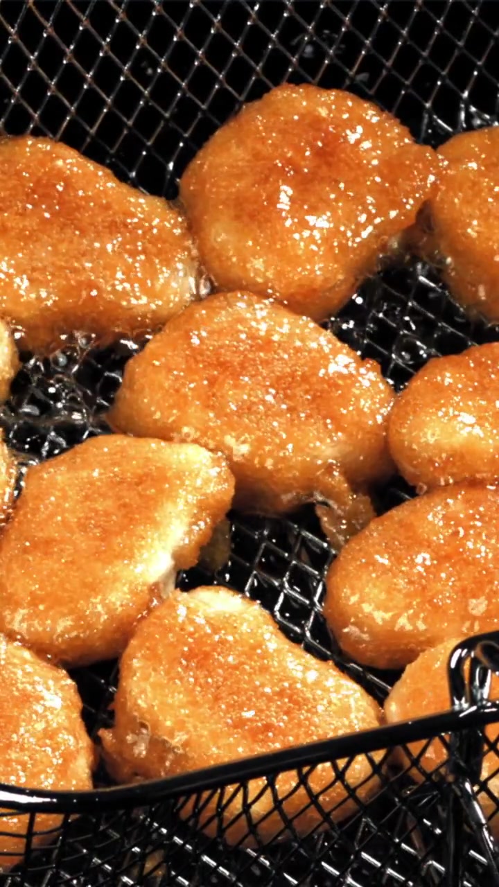フライヤーの熱い油で揚がるきつね色のチキンナゲット。