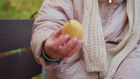 Close up of adult hand reaching into warm winter coat pocket to pull out fruit for child, gesture of care during cold autumn day, soft textures of scarf and jacket emphasize tenderness of moment