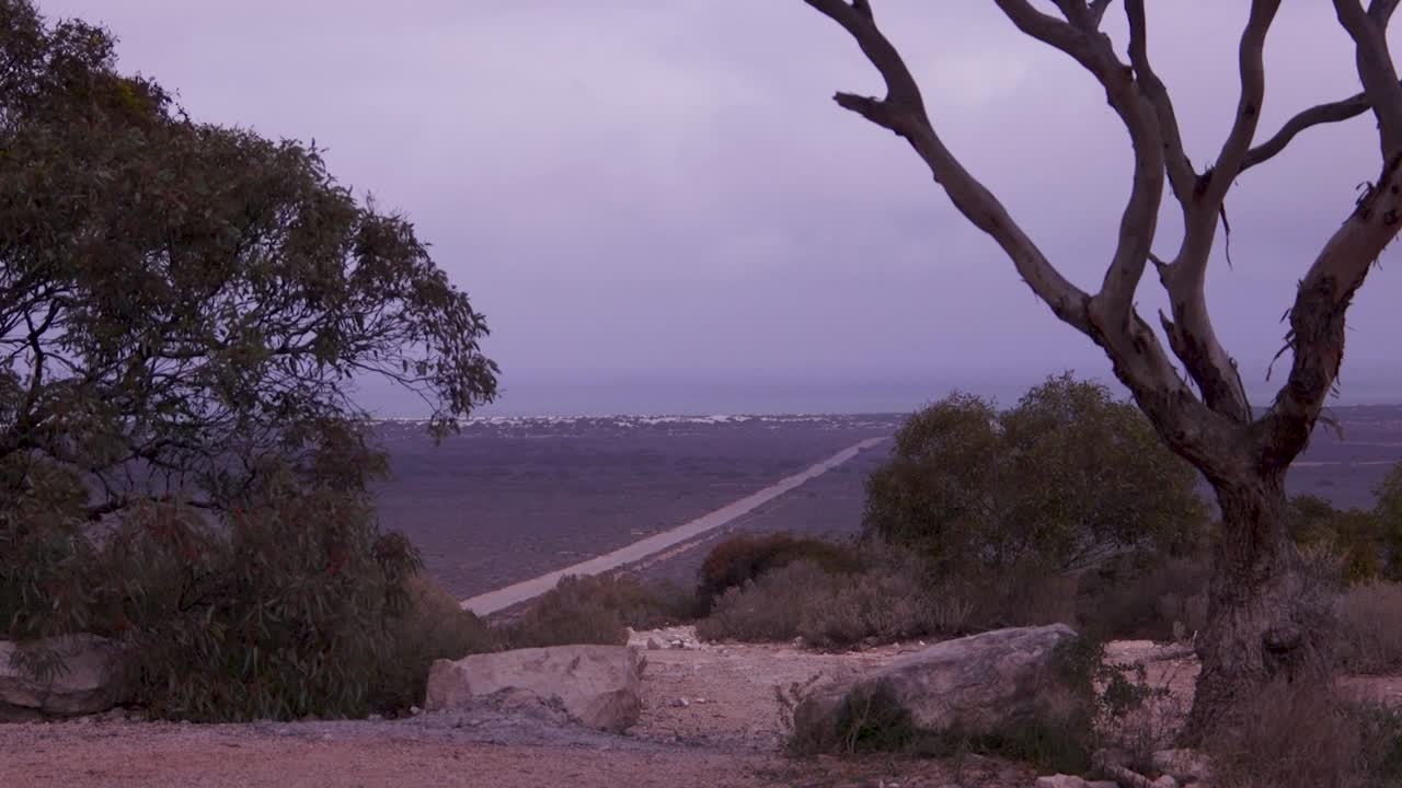 A solitary road extends through the expansive, moody landscape of Western Australia