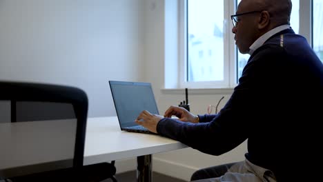 Schwarzer-Geschäftsmann-Arbeitet-Am-Laptop-Im-Büro-Am-Fenster