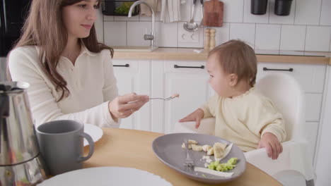 linda niña sentada en una silla alta en la cocina mientras su madre la alimenta