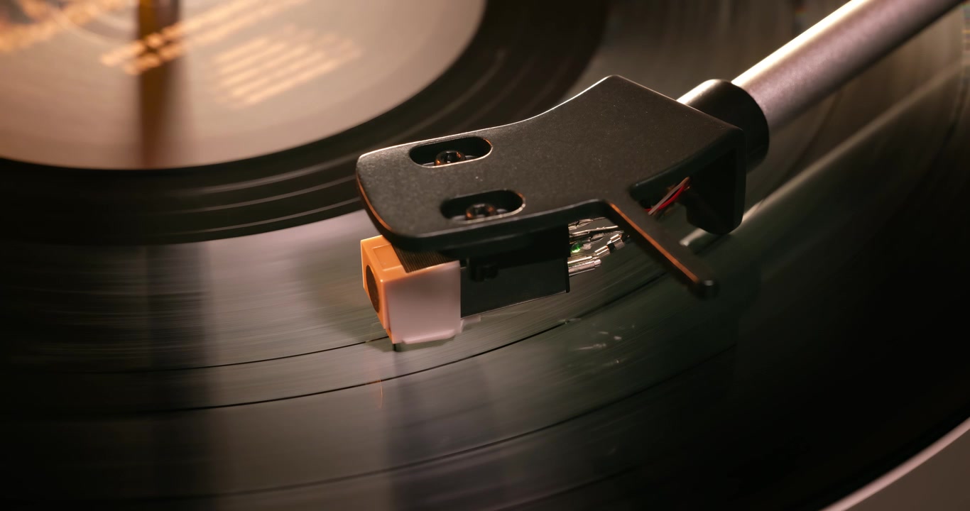 Primo piano dettagliato di un braccio di giradischi con portatestina bianco, posizionato su un disco in vinile nero sul piatto, che evidenzia la precisione dell'apparecchiatura audio.