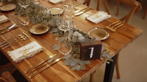 wooden wedding table set with gold cutlery and eucalyptus centerpiece