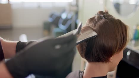 hands of caucasian male hairdresser highlighting female client's hair at salon, in slow motion