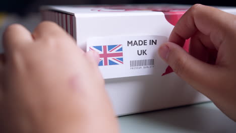 Hands-applying-MADE-IN-UK-flag-label-on-a-shipping-cardboard-box-with-products
