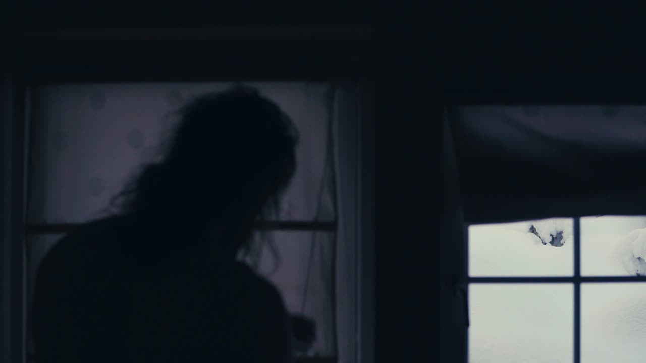 집에 있는 긴 머리의 남자는 겨울에 눈 덮인 풍경을 보기 위해 창문 덮개를 감는다