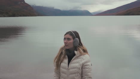 Woman in winter gear by a scenic lake with mountains