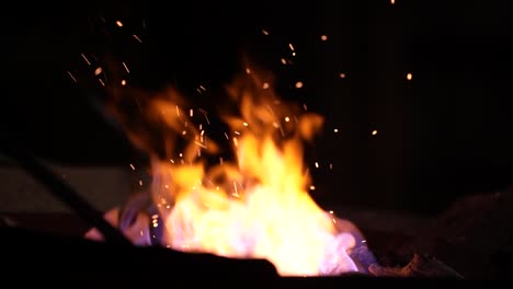 Flickering-Flames-on-the-Blacksmith's-Forge,-as-the-Foreground-Blurry-Hammer-Strikes-Iron-on-the-Anvil,-Crafting-Traditional-Handmade-Artifacts