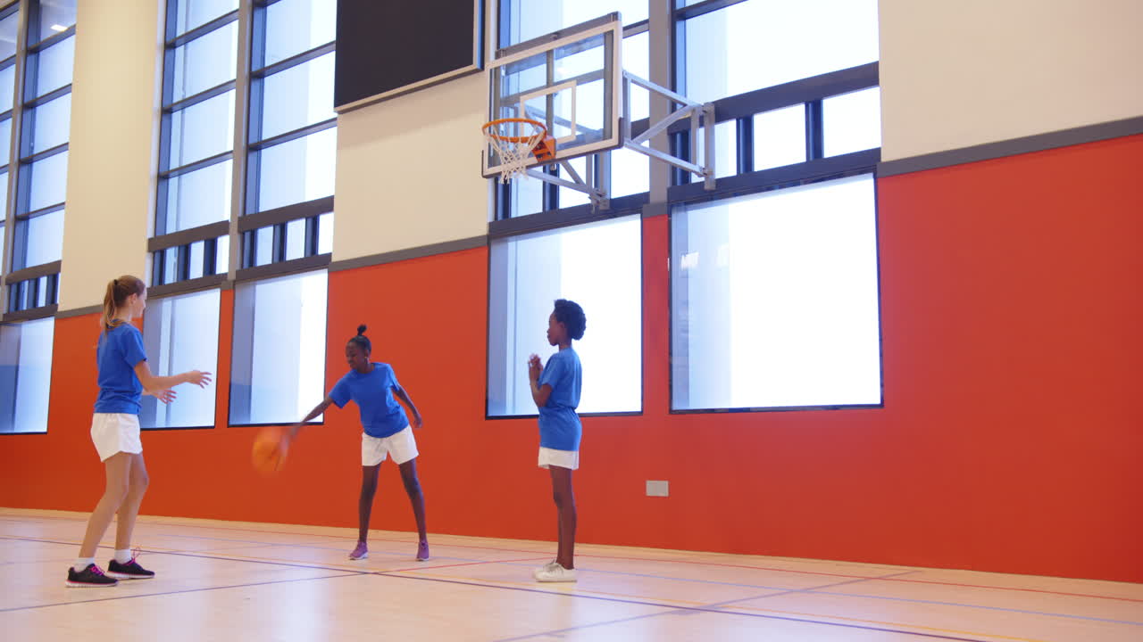Kinderen spelen basketbal in schoolgymzaal en oefenen schieten en passen.
