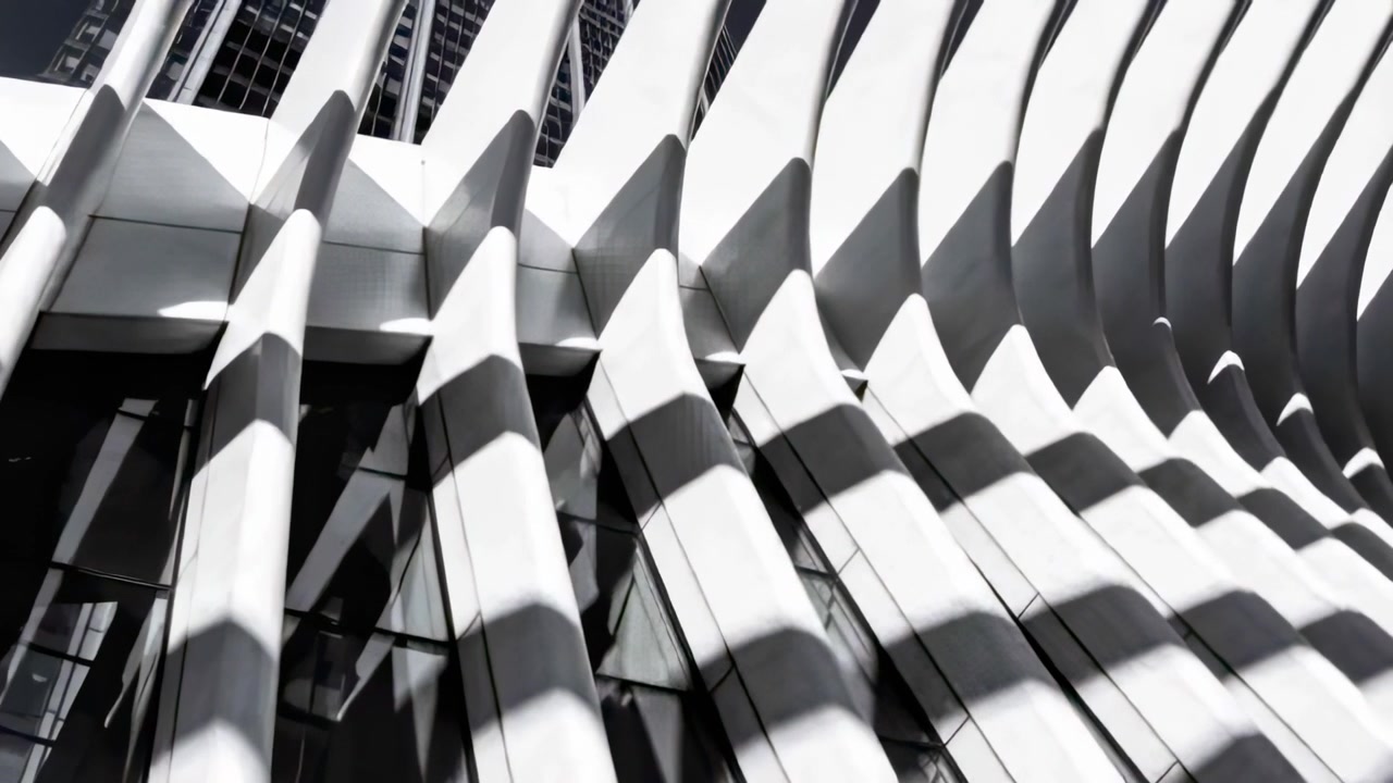 Sich bewegendes Sonnenlicht wirft diagonale Schatten über eine gerippte Fassade, die weiße Lamellen und Glas zeigt.