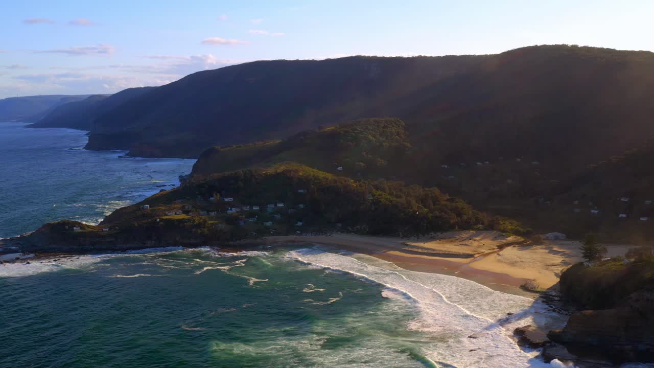 olas onduladas en la orilla arenosa de la playa de era con fondo de paisaje montañoso en verano en el parque nacional real, nueva gales del sur, australia