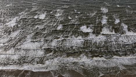wide aerial tilt down view of waves crashing on the beach with foam and sets of surf rolling in at sunset