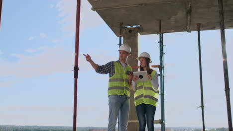 engineers builders man and woman standing on the roof of the building with a tablet computer discussing in white helmets and shirts.