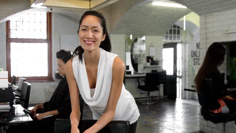 Smiling-female-hairstylist-leaning-on-chair