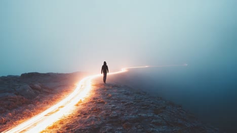 a solitary figure stands at the edge of a rocky pathway, shrouded in mist during twilight. the environment is ethereal, with soft light trails illuminating the winding path ahead. the atmosphere feels serene yet mysterious, evoking a sense of adventure and introspection. the combination of fog and d