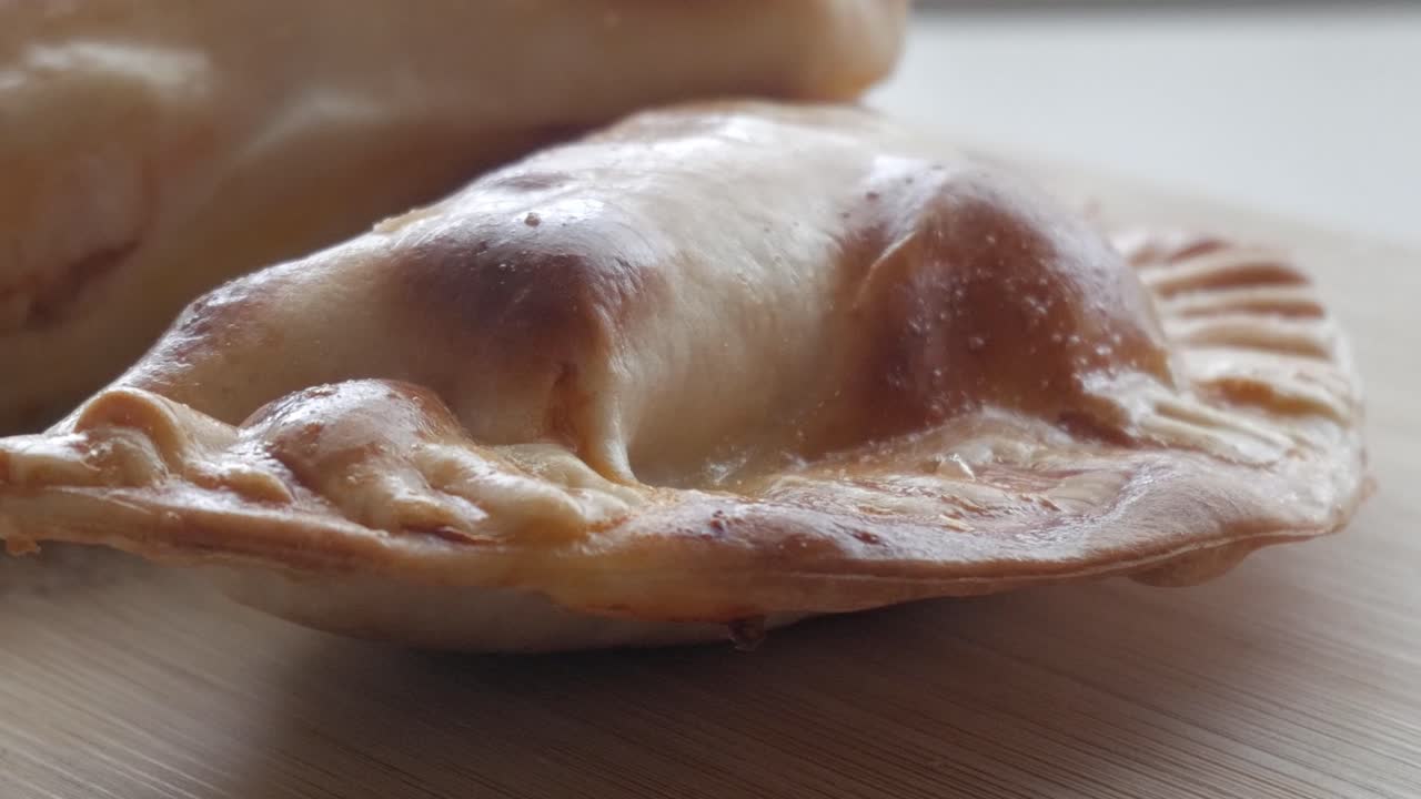 Golden-brown empanadillas on wooden surface, warm, homemade comfort food vibe