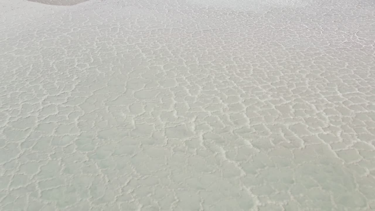Aerial view of salt flats in the Atacama Desert, Chile. The cracked white surface forms natural geometric patterns, highlighting the arid beauty and surreal atmosphere of the high desert