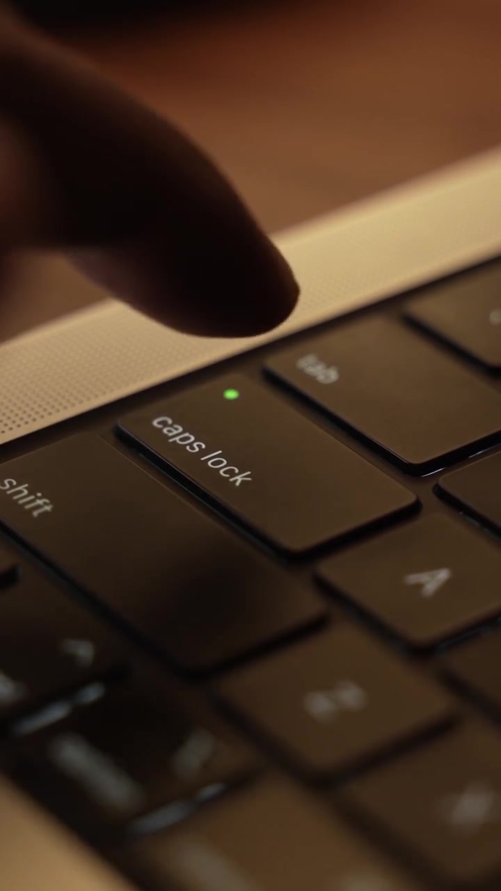 Finger trykker på Caps Lock-knappen på bærbar computers tastatur i et varmt oplyst rum