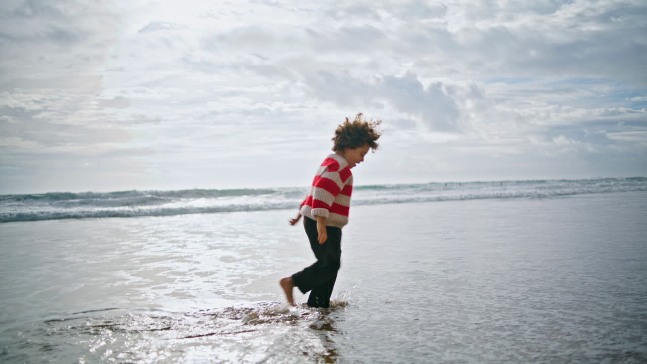 Happy kid walking ocean water in autumn sunlight. Joyful child playing waves