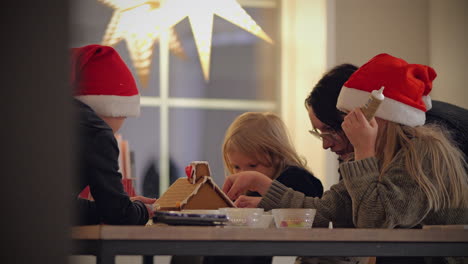 family decorating gingerbread house together at home during christmas, cozy and festive atmosphere