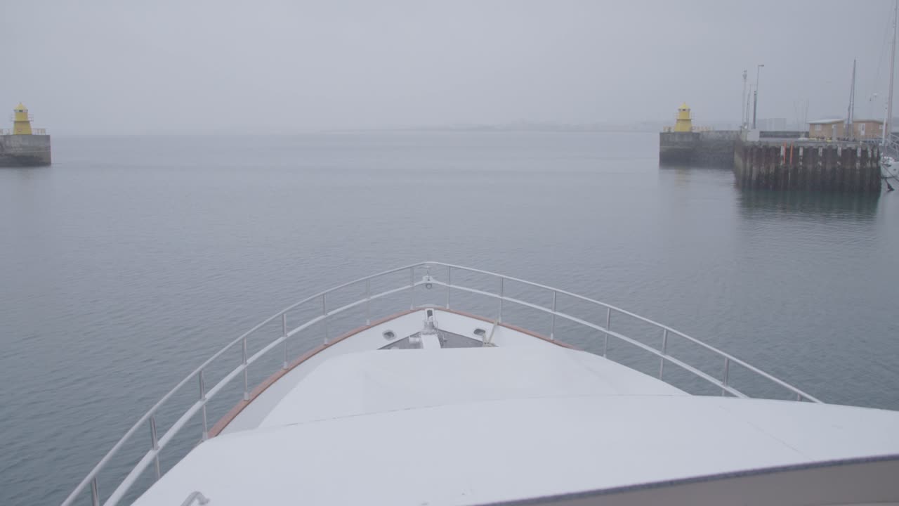 흐린 날에 항구를 떠나는 하얀 요트의 뱃머리를 바라보며 조타 장치에 서 있다