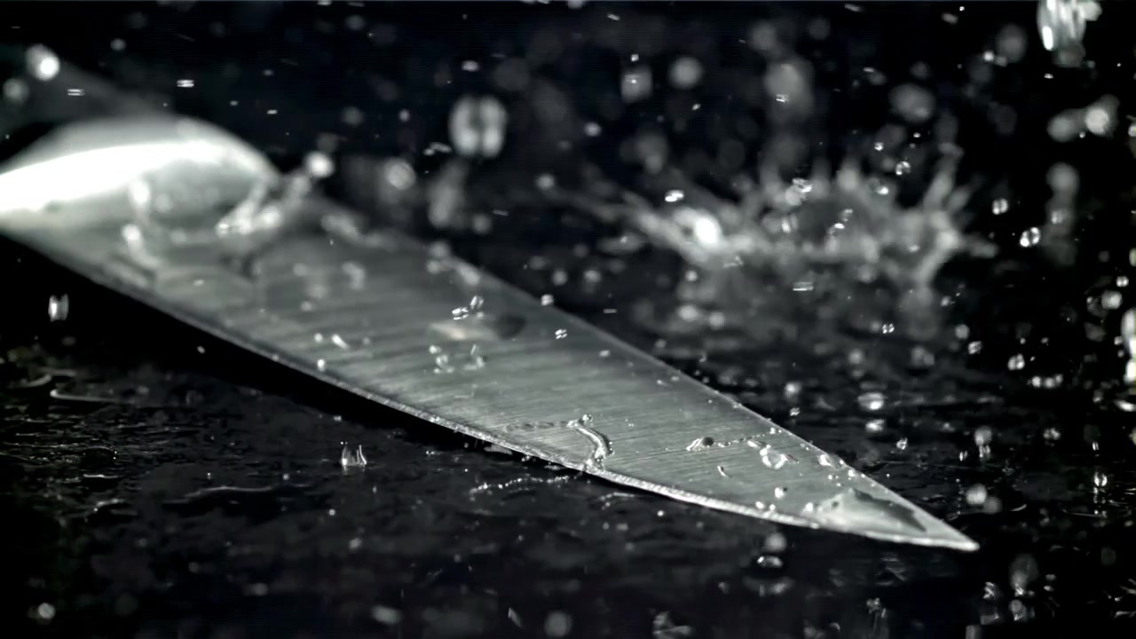 Vanddråber sprøjter på et skarpt knivblad i slowmotion.