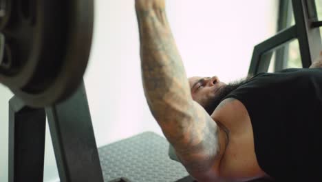 attractive sporty man with tattoos and beard at training bench press in gym close up