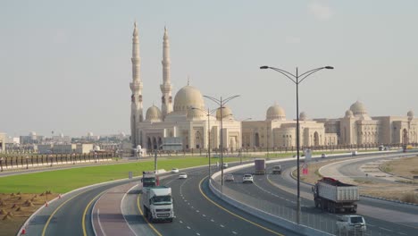 Coches-Que-Pasan-Por-Una-Vía-Urbana-Con-La-Mezquita-De-La-Universidad-Al-Qasimia-Al-Fondo-En-Sharjah,-Emiratos-árabes-Unidos