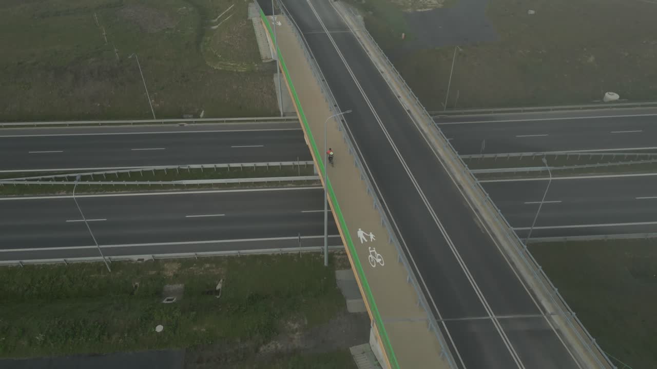 Cyclist crosses an empty overpass over a highway in the early morning fog, aerial view
