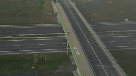 cyclist crosses an empty overpass over a highway in the early morning fog, aerial view