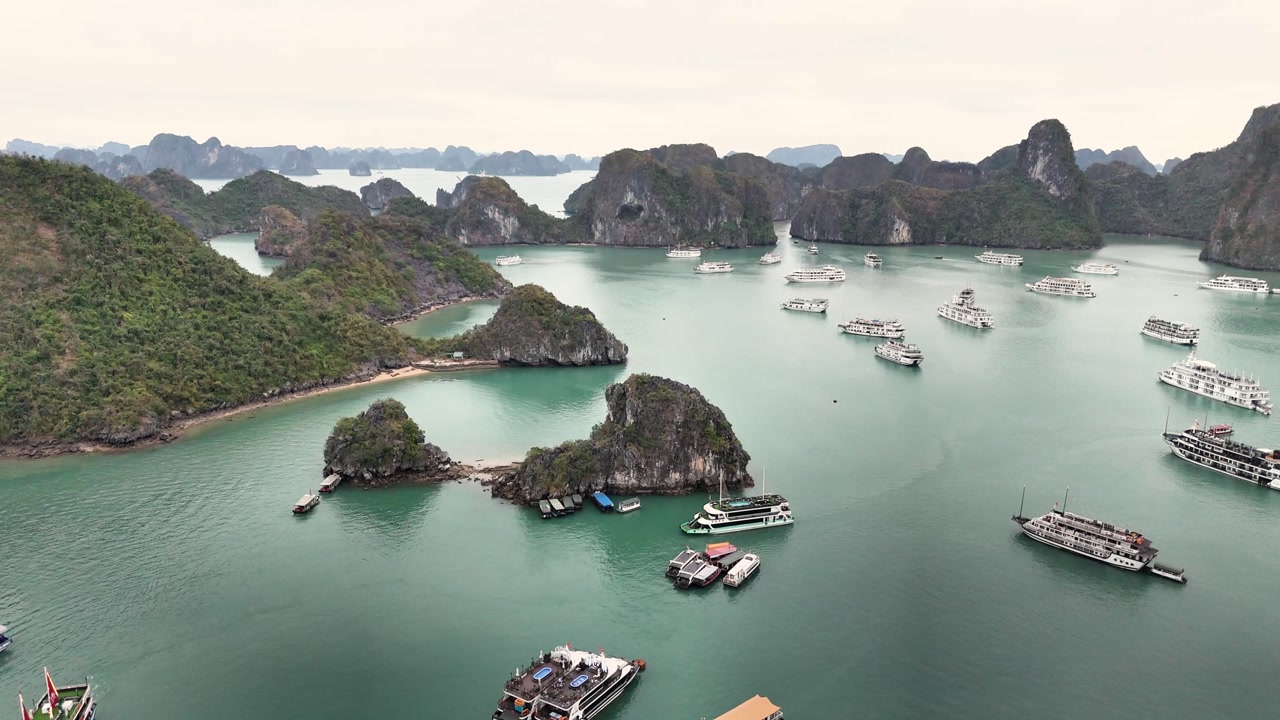 Smooth aerial glide above Ha Long Bay, Vietnam, showcasing emerald waters, limestone karst islands, and numerous tourist cruise boats scattered across the bay.