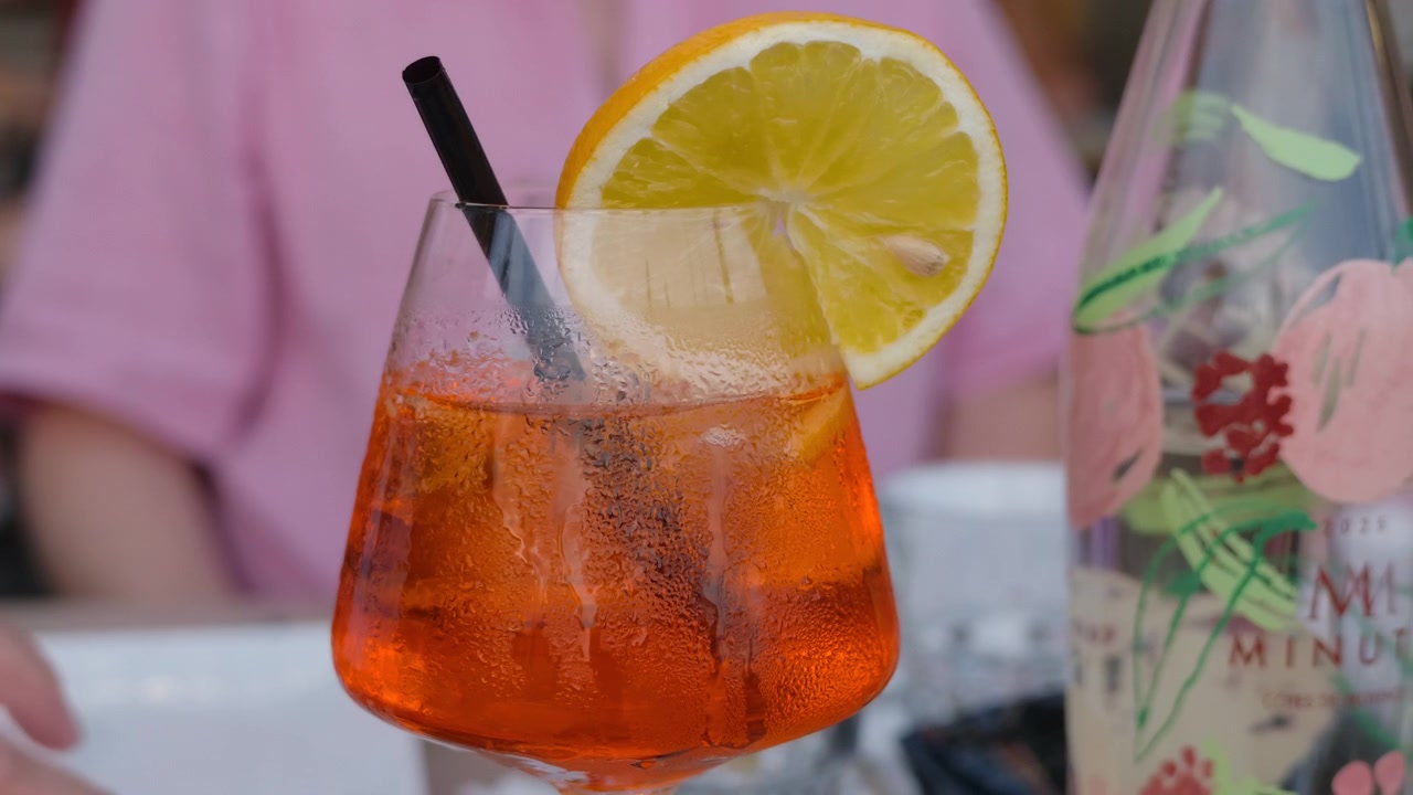 Primo piano di un cocktail spritz arancione accanto a una bottiglia decorata.