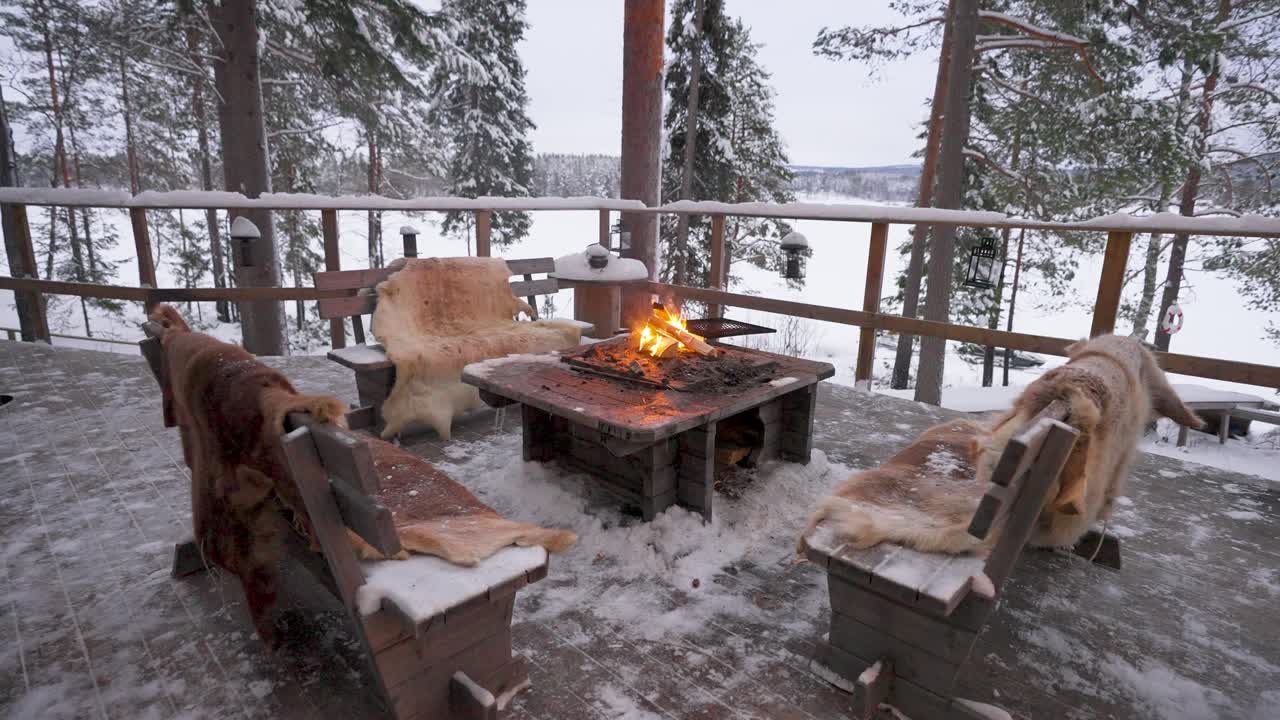 A warm and inviting fire burns brightly in the middle of a cosy log cabin in Sweden. Benches surround the fire, creating the perfect setting for relaxation in a winter wonderland.