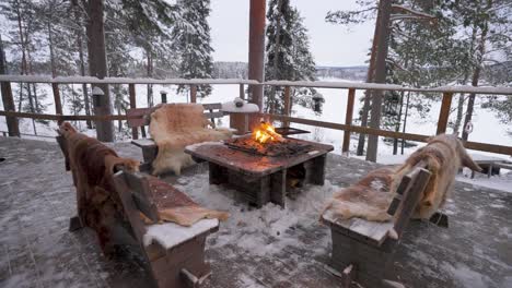 a warm and inviting fire burns brightly in the middle of a cosy log cabin in sweden. benches surround the fire, creating the perfect setting for relaxation in a winter wonderland.