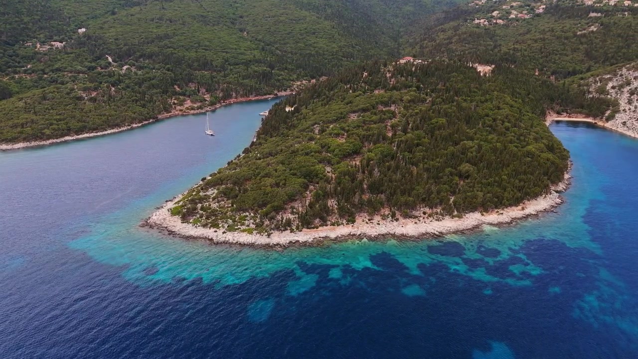 Vista aerea 4K di una barca a vela solitaria ancorata in una baia turchese cristallina circondata da foreste a Evreti, Isola di Cefalonia, Grecia