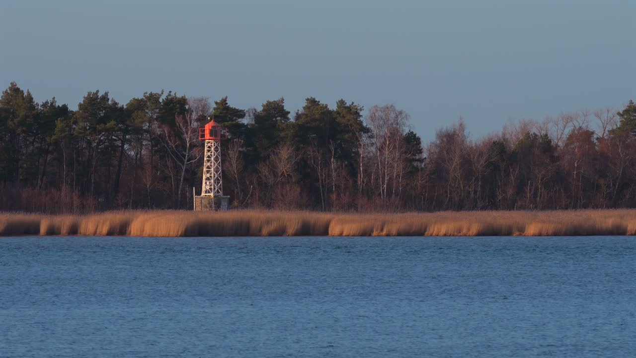 Kopuła radaru o zachodzie słońca, z głęboką niebieską wodą i trzcinami na pierwszym planie.