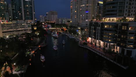 Aerial-approaching-shot-of-train-on-track-and-boat-on-river-in-american-city-at-night