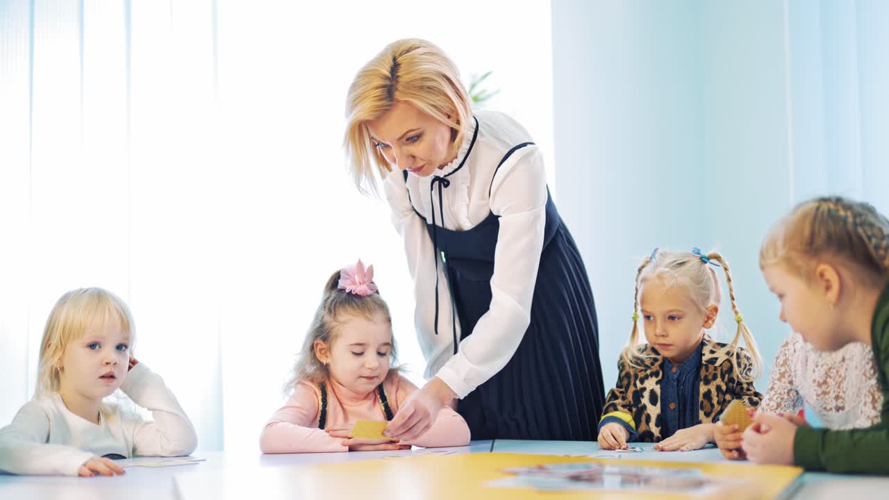 Teacher and little girls in class. Creative teacher wearing classical clothing explains the rules of game to children during the lesson. Elementary school inside.