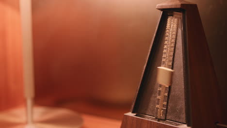 Dusty-metronome-that-is-moving-back-and-forth-on-a-lamp-lit-shelf