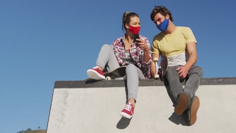 Amigos-Caucásicos-De-Mujer-Y-Hombre-Con-Mascarilla,-Sentados-Y-Usando-Un-Teléfono-Inteligente