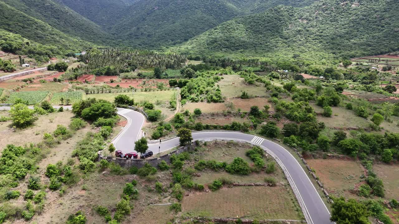 Mesmerizing drone footage of a scenic journey on a mountain road. Captures a series of hairpin bends ascending through vibrant green hillside fields. Perfect for road trip and adventure themes